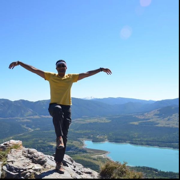 Arms spread on a rocky summit above a turquoise lake